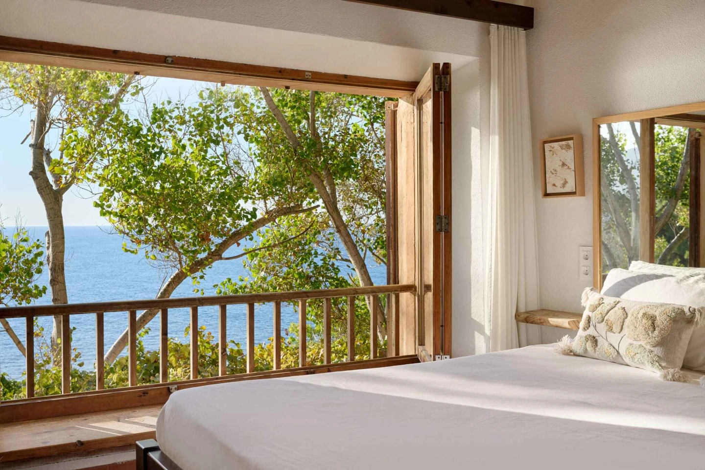 An inside view from a bedroom, showcasing a view of the ocean through trees,
